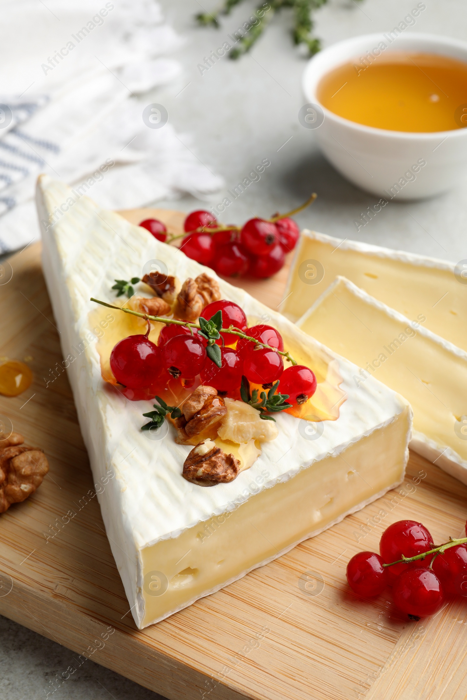 Photo of Brie cheese served with red currants, walnuts and honey on table, closeup