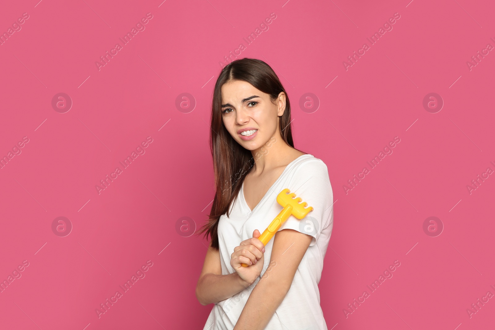 Photo of Young woman scratching arm with toy rake on color background. Annoying itch