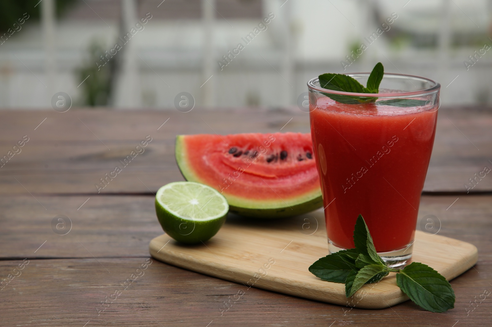 Photo of Glass of delicious watermelon smoothie with mint and fresh cut fruits on wooden table. Space for text