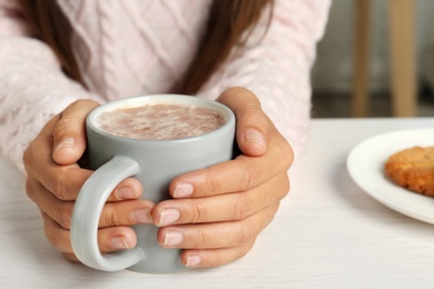 Photo of Woman holding cup of delicious cocoa drink at white table, closeup