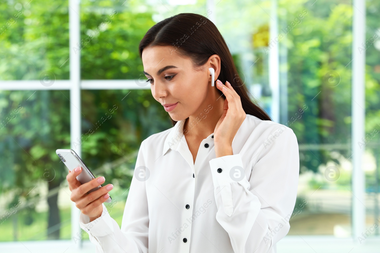 Photo of Young woman with smartphone listening to music through wireless earphones indoors