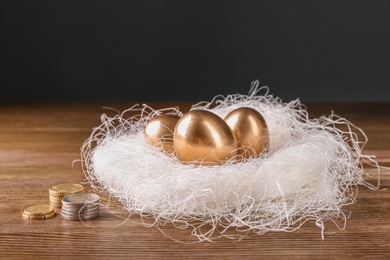 Photo of Golden eggs in nest and coins on wooden table. Pension planning