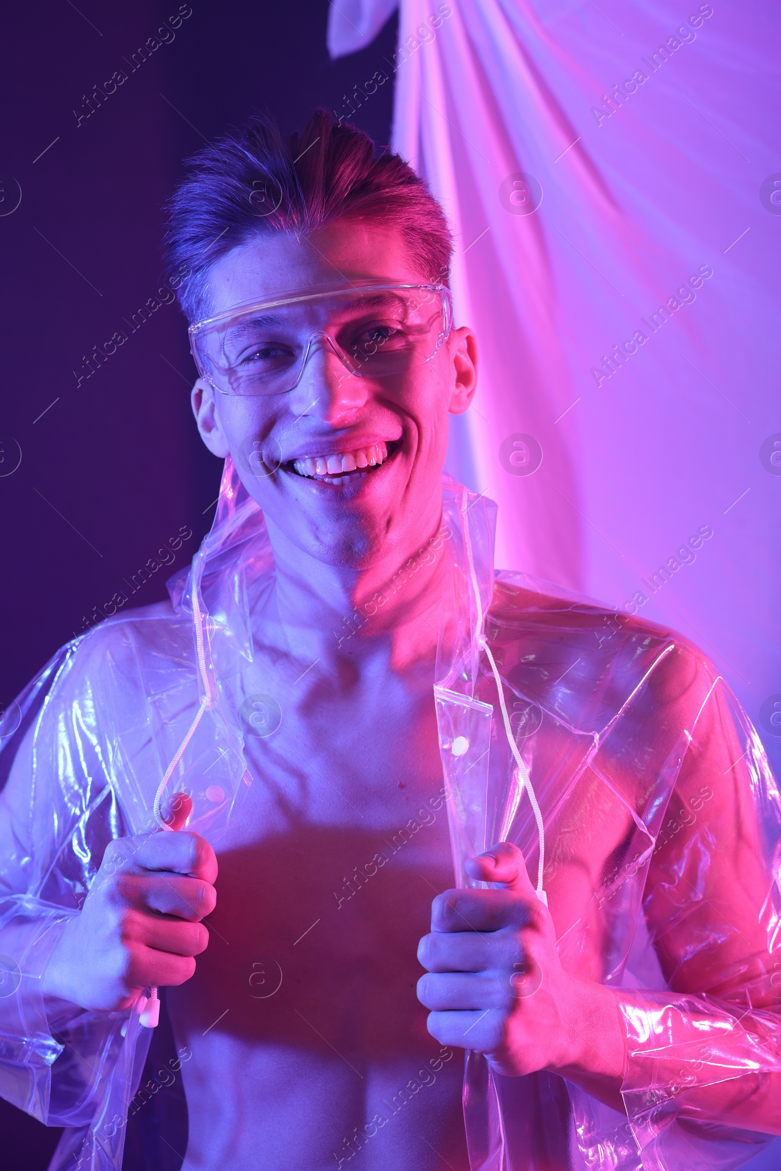 Photo of Stylish young man wearing clear coat and glasses in neon lights