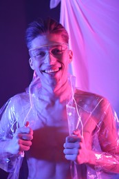 Photo of Stylish young man wearing clear coat and glasses in neon lights