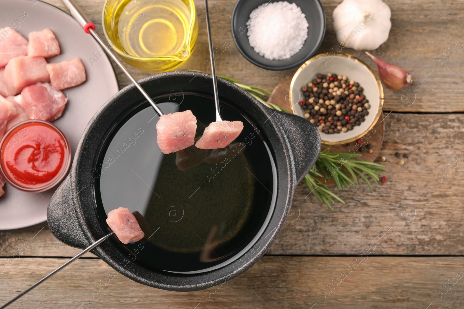 Photo of Fondue pot with oil, forks, raw meat pieces and other products on wooden table, flat lay