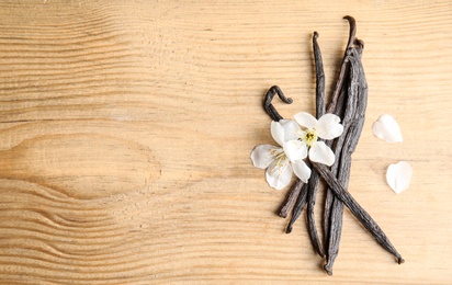 Photo of Flat lay composition with aromatic vanilla sticks and flowers on wooden background. Space for text