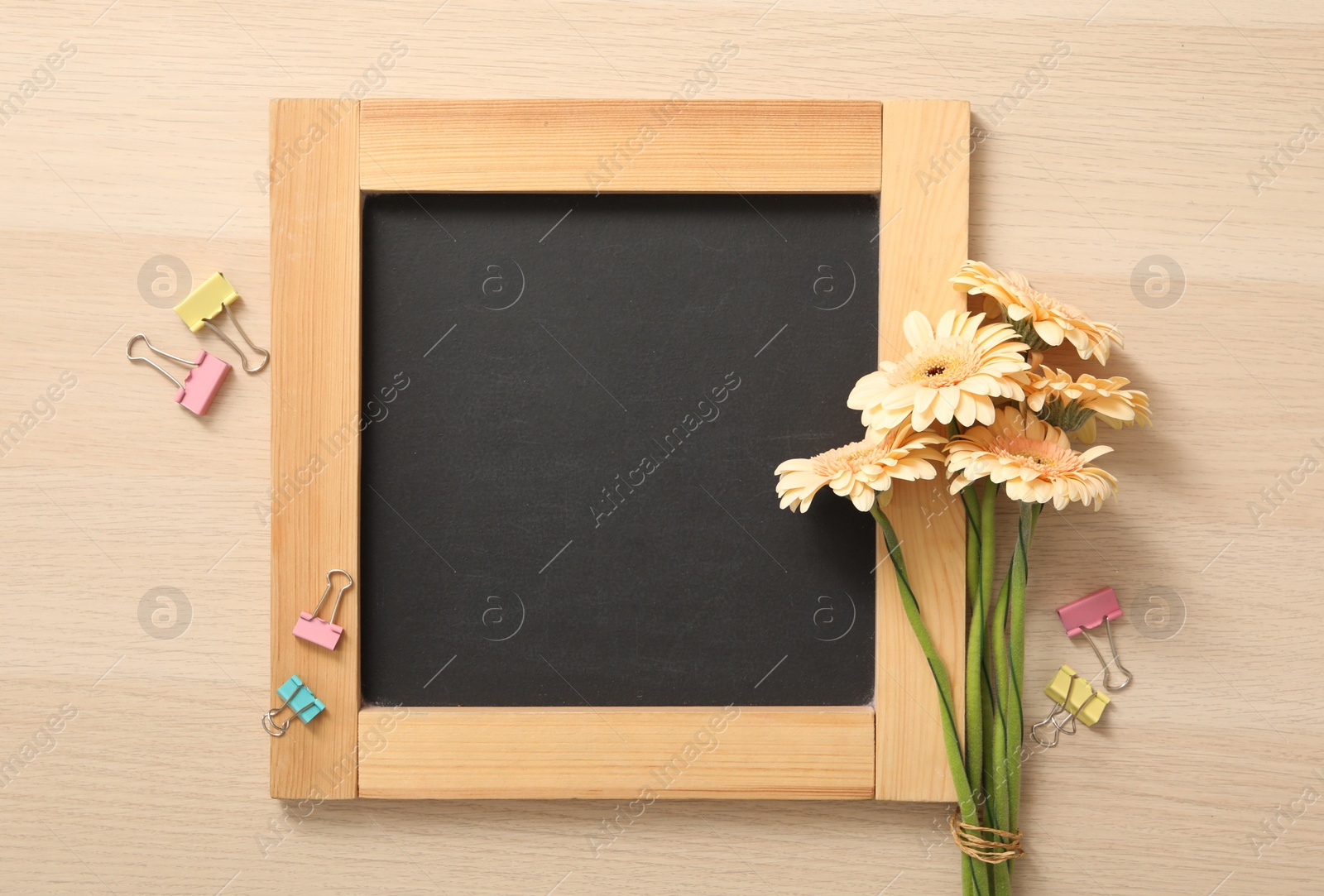 Photo of Blackboard, paper clips and flowers on wooden table, flat lay with space for text. Teacher's Day