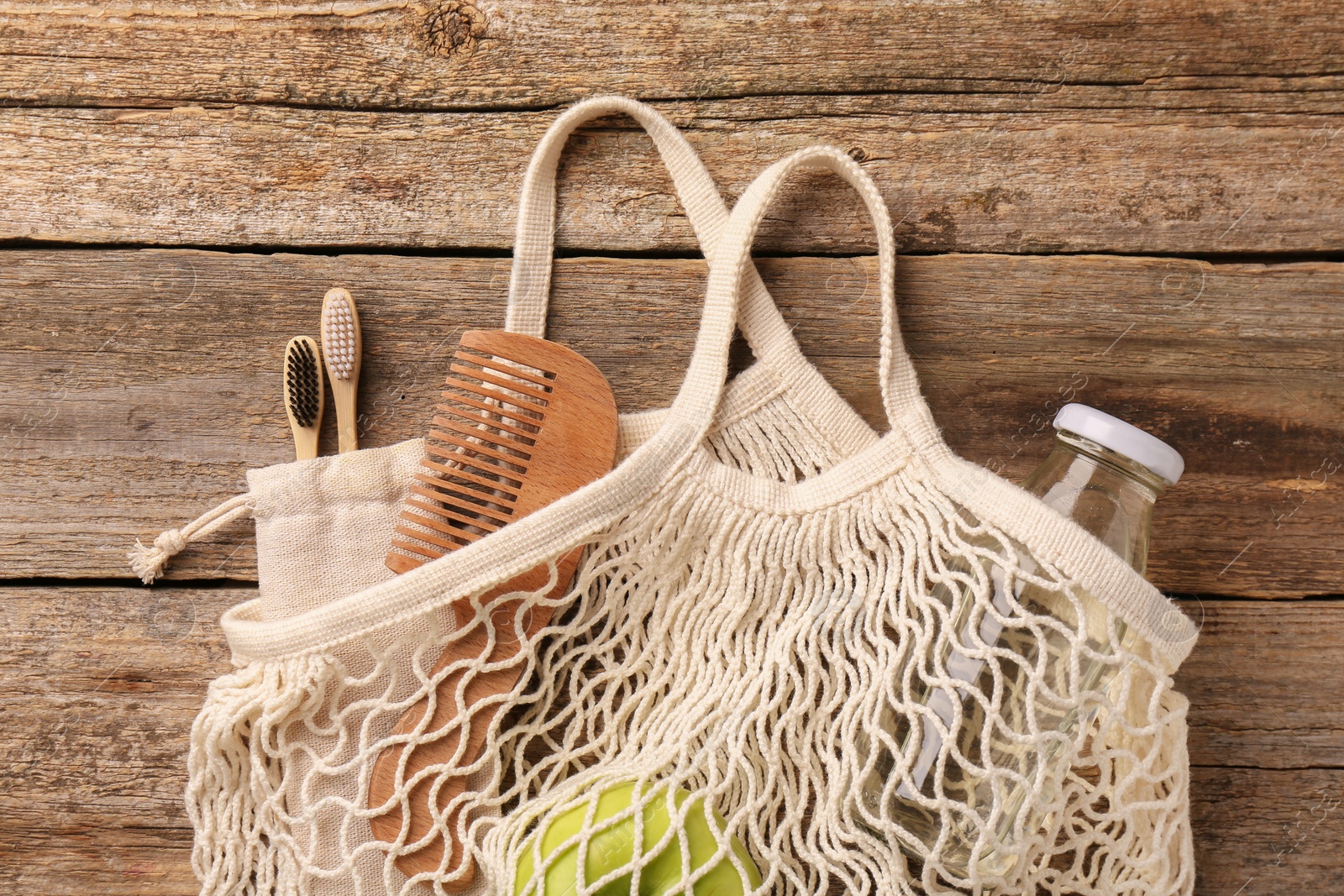 Photo of Net bag with different items on wooden table, top view. Conscious consumption