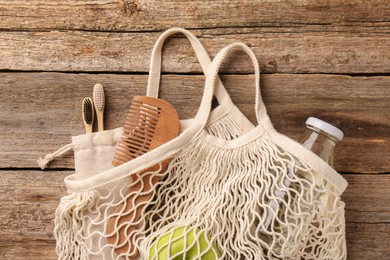 Net bag with different items on wooden table, top view. Conscious consumption
