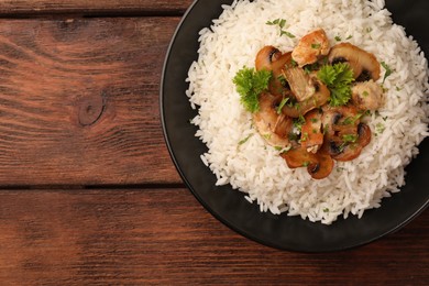 Delicious rice with mushrooms and parsley on wooden table, top view. Space for text