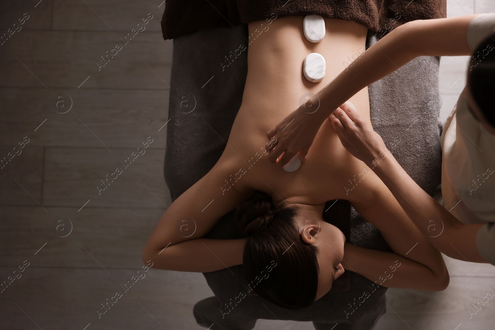 Photo of Spa therapy. Beautiful young woman lying on table during hot stone massage in salon, top view. Space for text