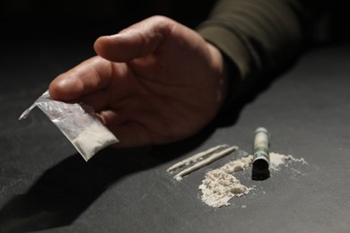 Photo of Drug addiction. Man with cocaine and rolled dollar banknote at grey table, closeup