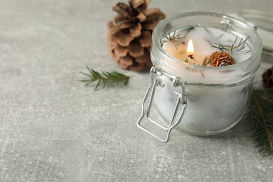 Burning scented conifer candle and Christmas decor on grey table. Space for text