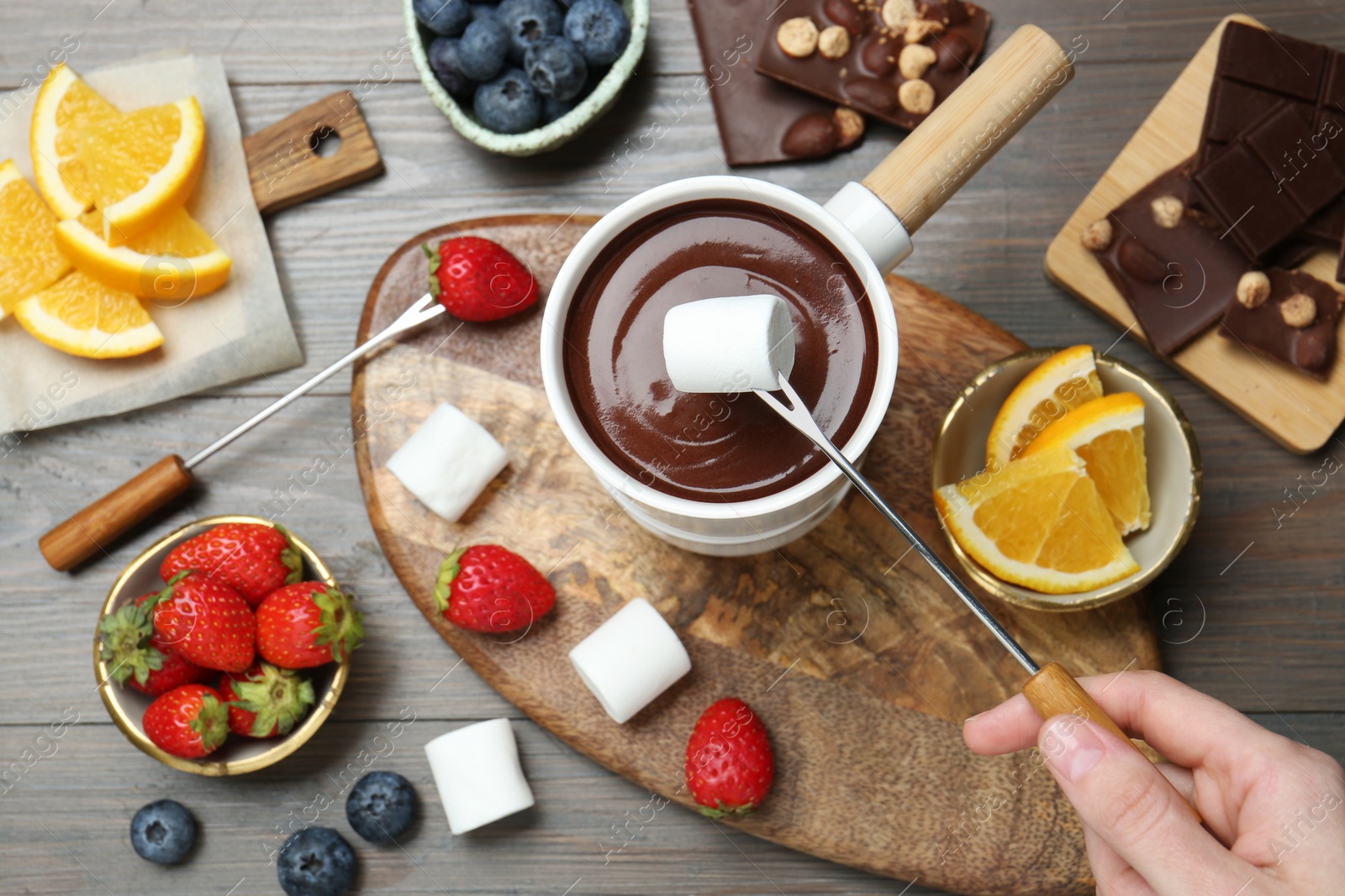 Photo of Woman dipping sweet marshmallow in fondue pot with melted chocolate at wooden table, top view