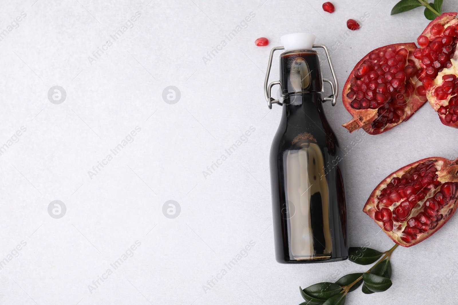 Photo of Tasty pomegranate sauce in bottle, branches and cut fruit on light table, flat lay. Space for text