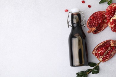 Photo of Tasty pomegranate sauce in bottle, branches and cut fruit on light table, flat lay. Space for text