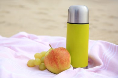 Photo of Metallic thermos with hot drink, fruits and plaid on sandy beach, closeup