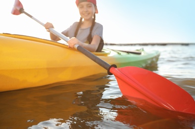 Photo of Little girl kayaking along river, focus on paddle. Summer camp activity