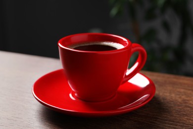 Photo of Red cup with aromatic coffee on wooden table indoors, closeup