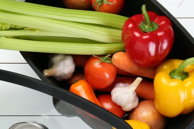 Photo of Black pot with fresh vegetables and glass lid on white wooden table, top view