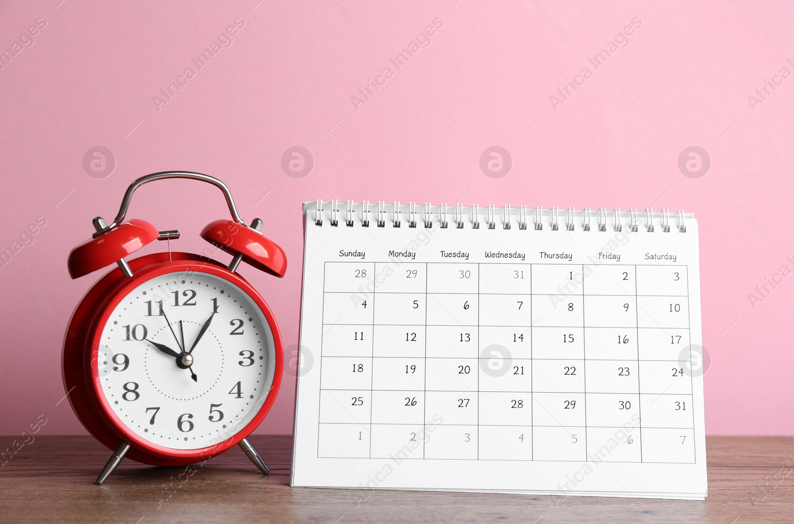 Photo of Calendar and alarm clock on wooden table against pink background