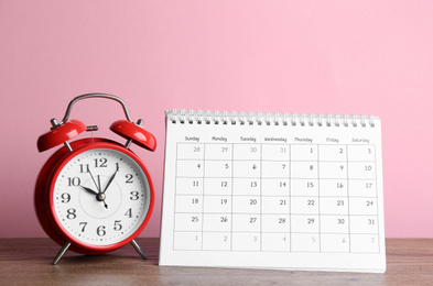 Photo of Calendar and alarm clock on wooden table against pink background