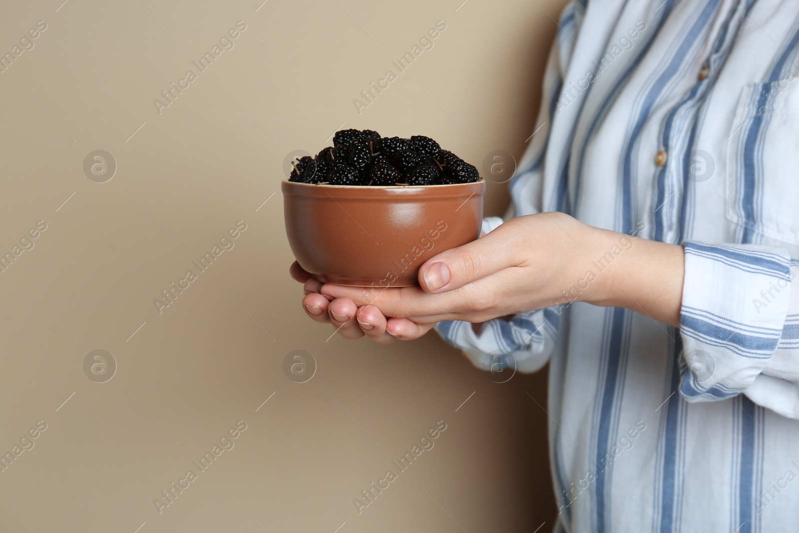 Photo of Woman holding bowl of fresh ripe black mulberries on light grey background, closeup. Space for text