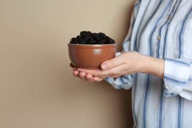 Woman holding bowl of fresh ripe black mulberries on light grey background, closeup. Space for text