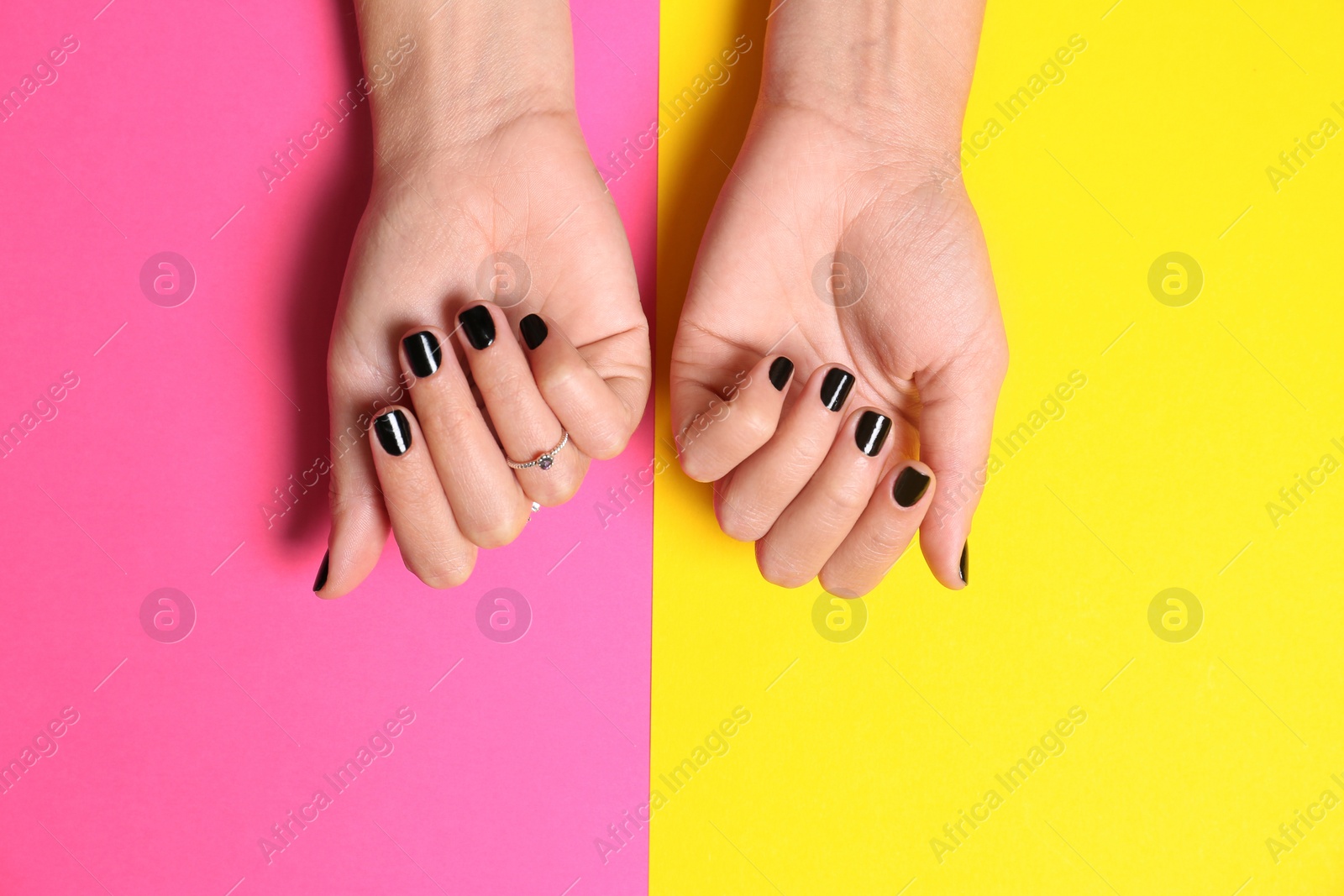 Photo of Woman showing manicure with black nail polish on color background, top view