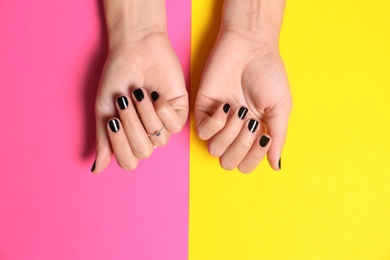 Woman showing manicure with black nail polish on color background, top view