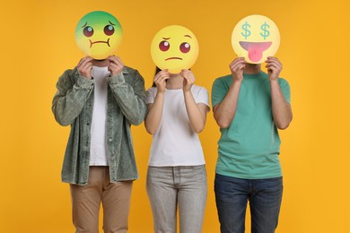 People covering faces with emoticons on yellow background