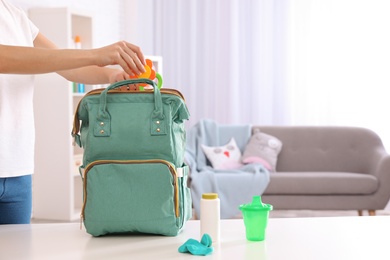 Photo of Woman packing baby accessories into maternity backpack on table indoors, closeup