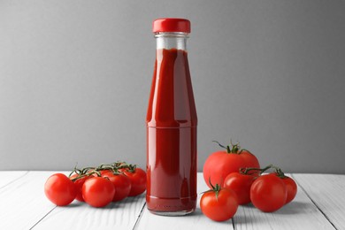 Photo of Bottle of tasty ketchup and tomatoes on white wooden table