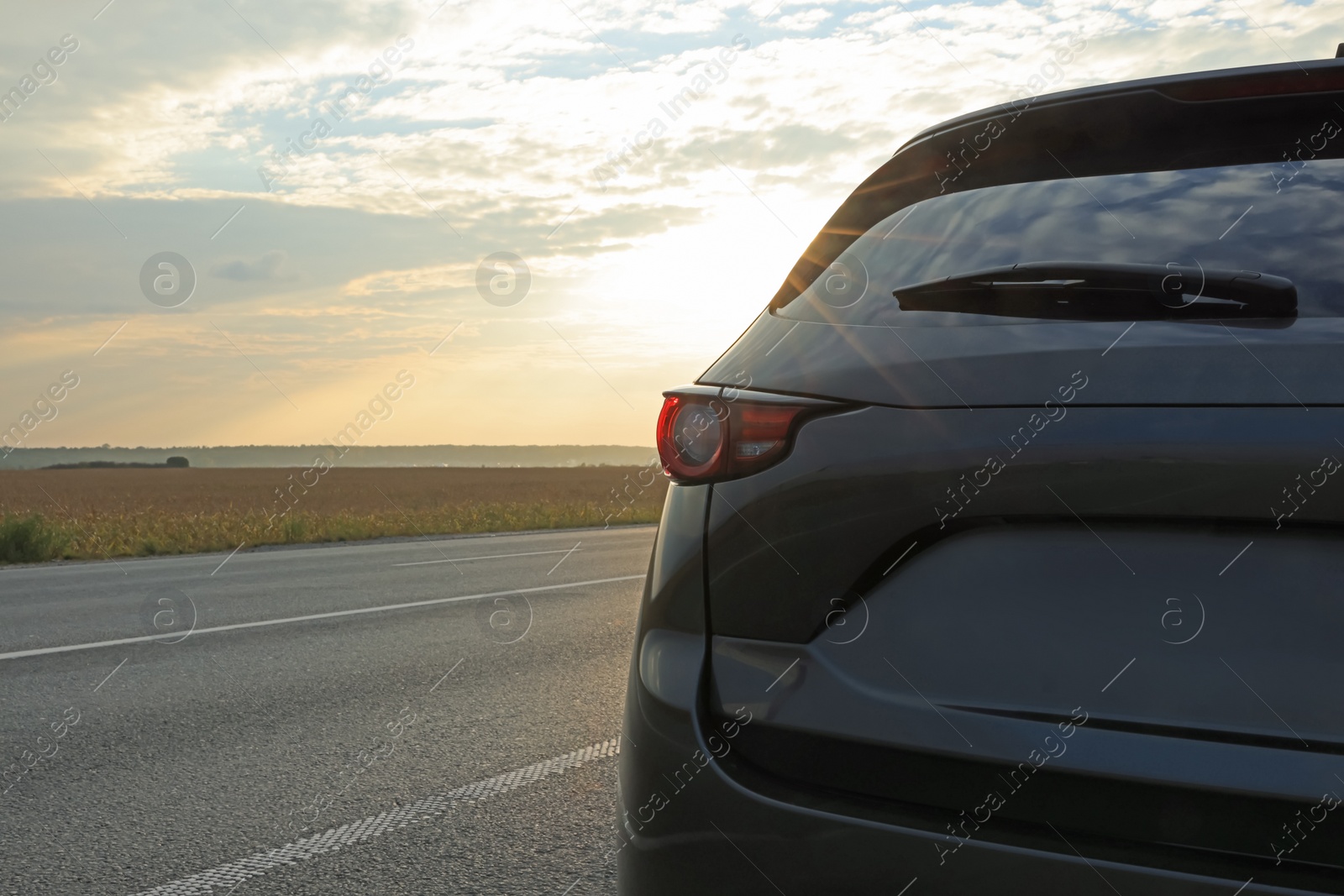 Photo of Black modern car parked on road at sunset, closeup. Space for text