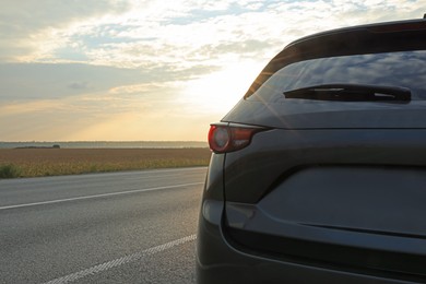 Photo of Black modern car parked on road at sunset, closeup. Space for text
