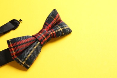 Photo of Stylish tartan bow tie on yellow background, closeup. Space for text