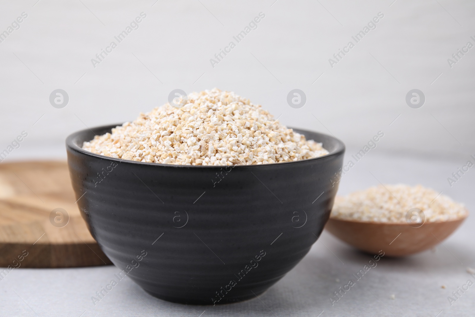 Photo of Dry barley groats in bowl and spoon on light grey table, closeup