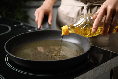 Photo of Woman pouring cooking oil from bottle into frying pan, closeup