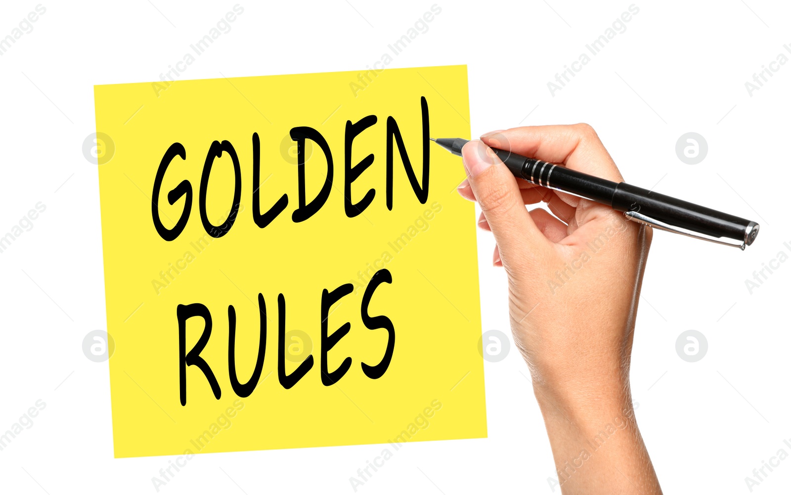 Image of Young woman writing phrase GOLDEN RULES on yellow note against white background, closeup