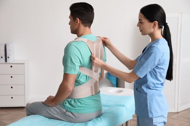Photo of Orthopedist helping patient to put on posture corrector in clinic. Scoliosis treatment