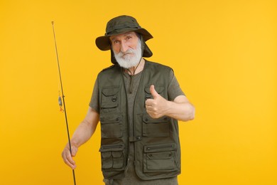 Photo of Fisherman with fishing rod showing thumb up on yellow background