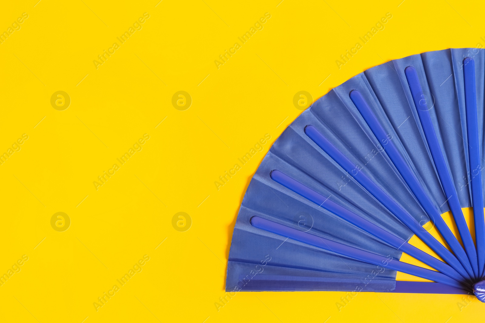 Photo of Blue hand fan on yellow background, top view. Space for text