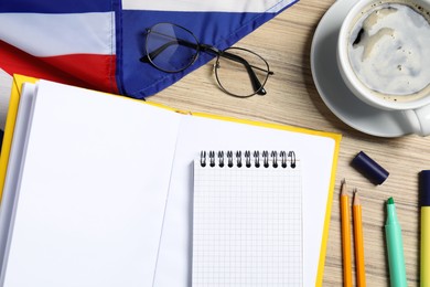 Learning foreign language. Open book, flag of United Kingdom, stationery and glasses on wooden table, flat lay