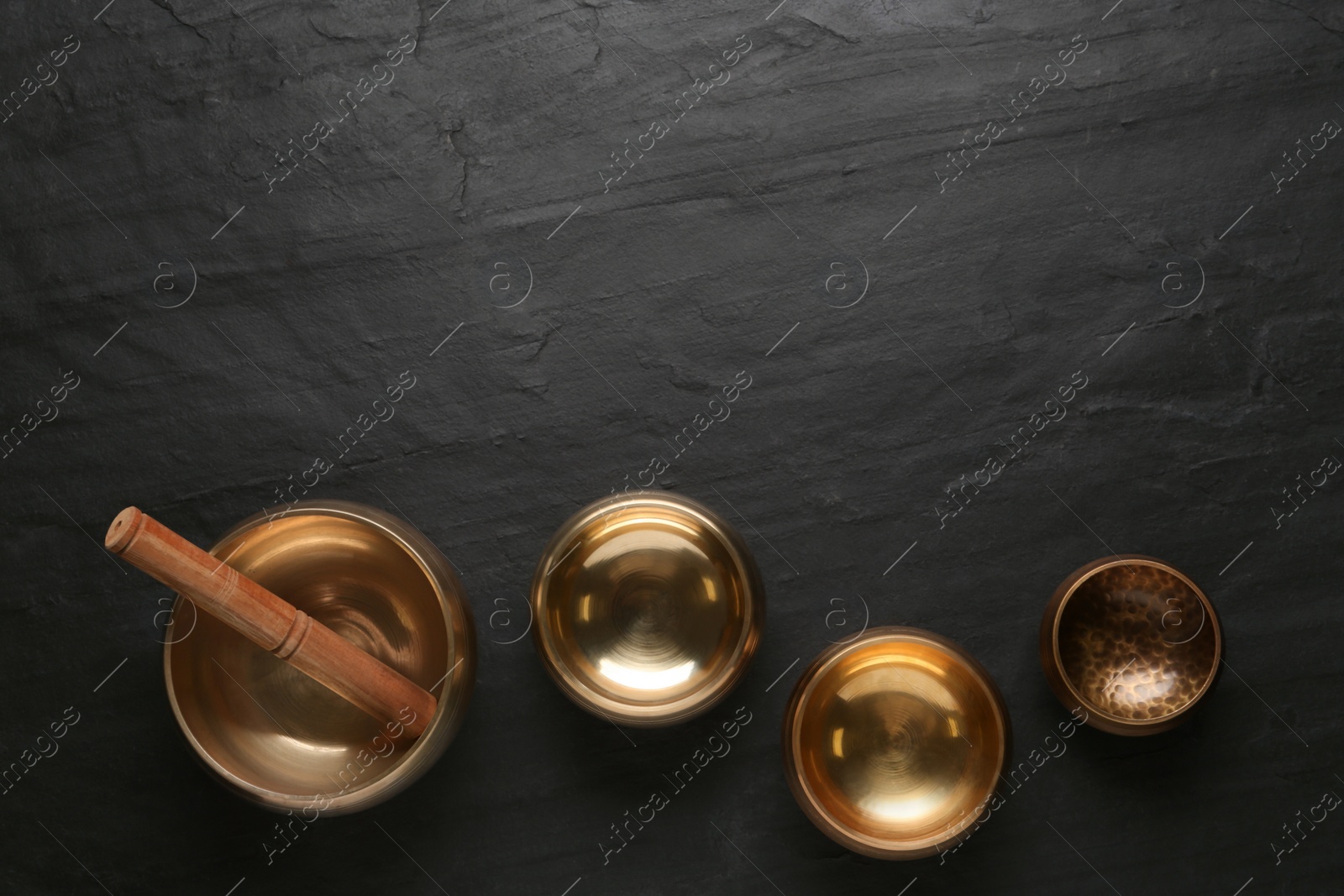 Photo of Golden singing bowls and mallet on black table, flat lay. Space for text