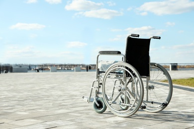 Photo of Empty wheelchair outdoors on sunny day. Space for text