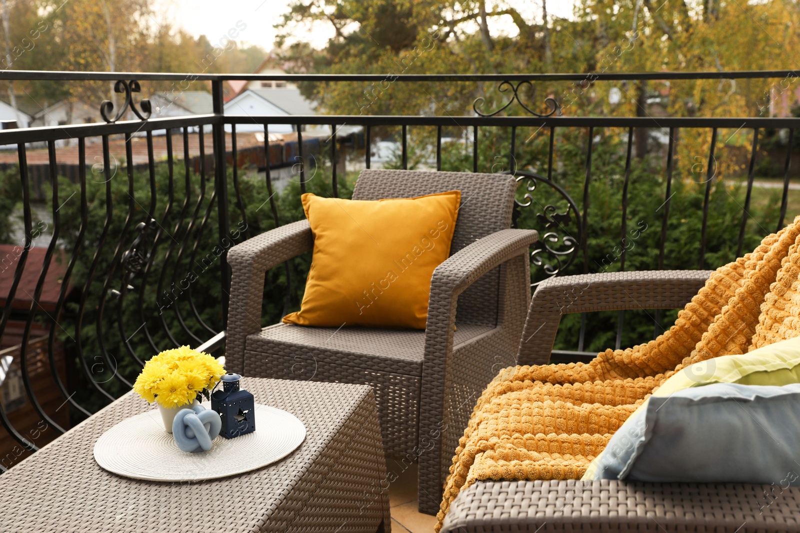 Photo of Colorful pillows, soft blanket and yellow chrysanthemum flowers on rattan garden furniture outdoors