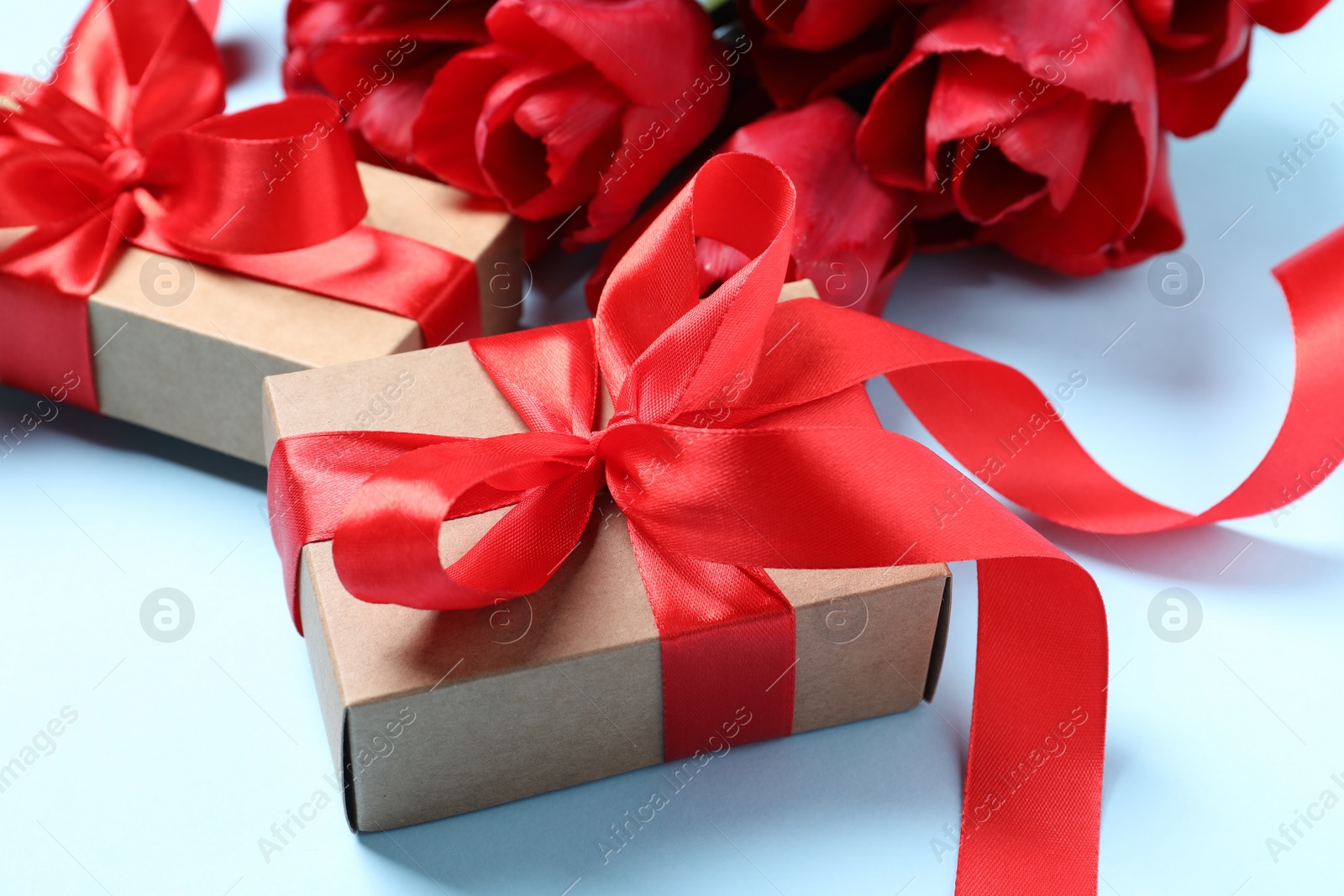 Photo of Beautiful gift box and red tulip flowers on light blue background, closeup