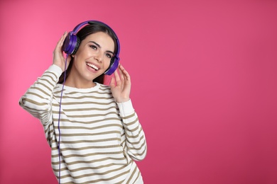 Attractive young woman enjoying music in headphones on color background. Space for text