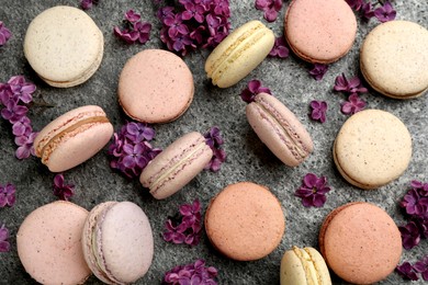 Photo of Delicious macarons and flowers on grey table, flat lay