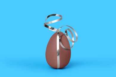 Photo of Delicious chocolate egg with silver ribbon on light blue background